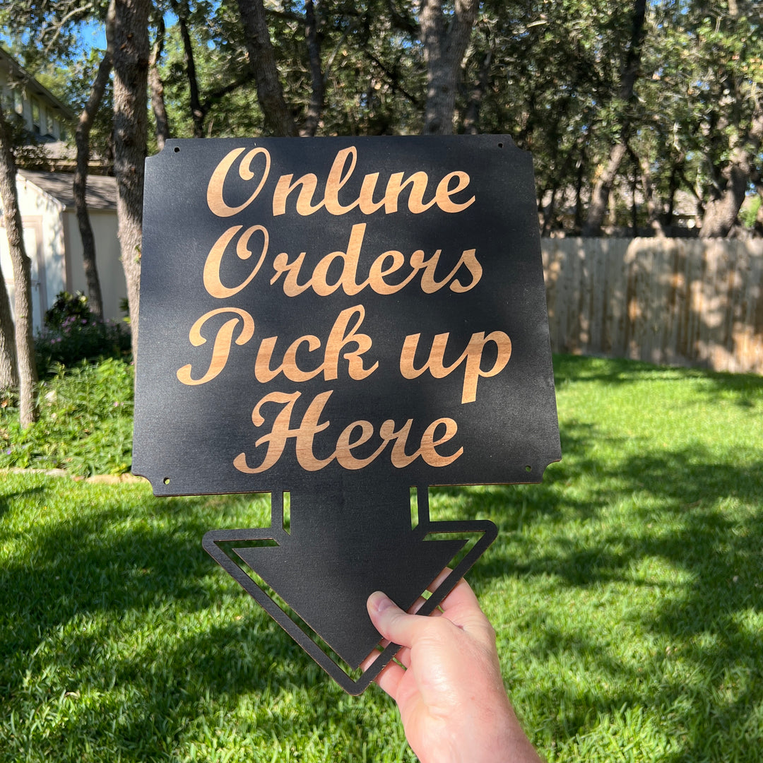 Hand holding a HipFlaskPlus Online Orders Pick Up Here black wood arrow sign on grass