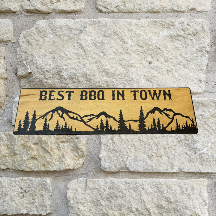 HipFlaskPlus Best BBQ in Town mountain scene black and natural wood sign on a stone wall