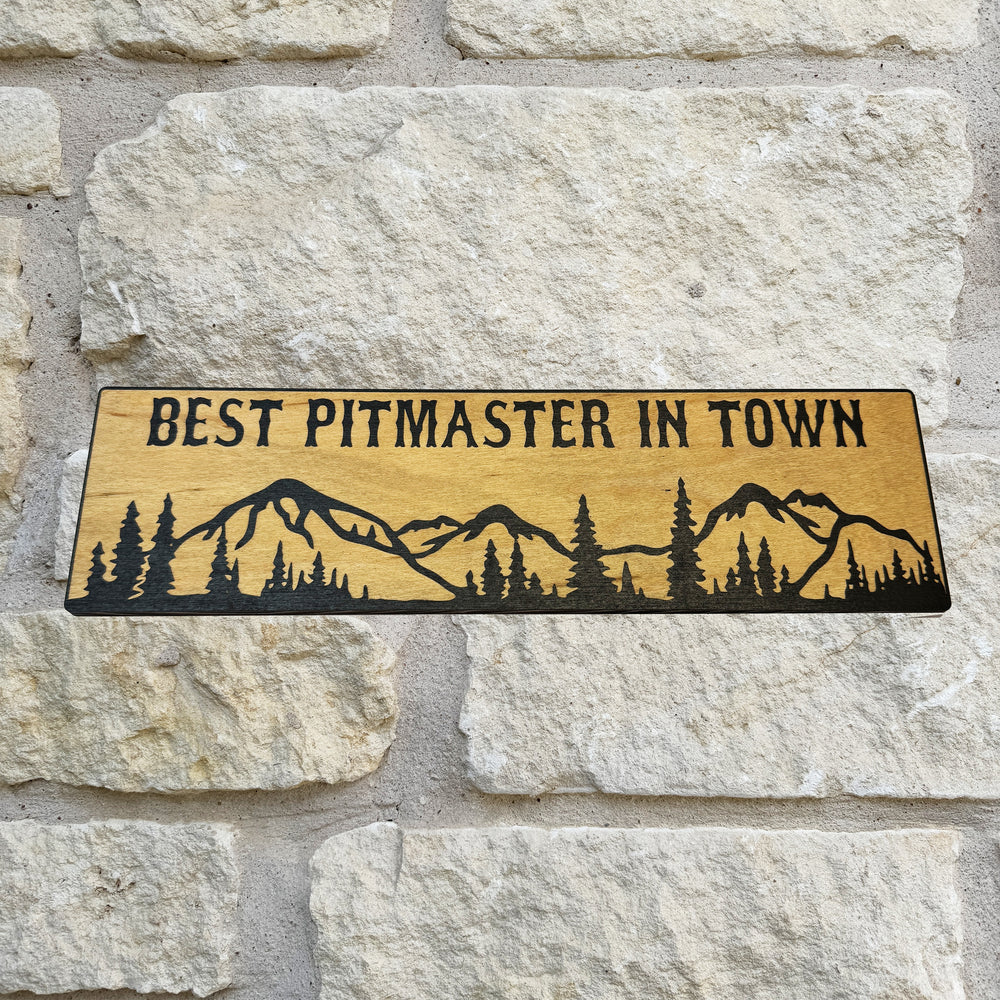 HipFlaskPlus Best Pitmaster in Town mountain scene black and natural wood sign on a stone wall