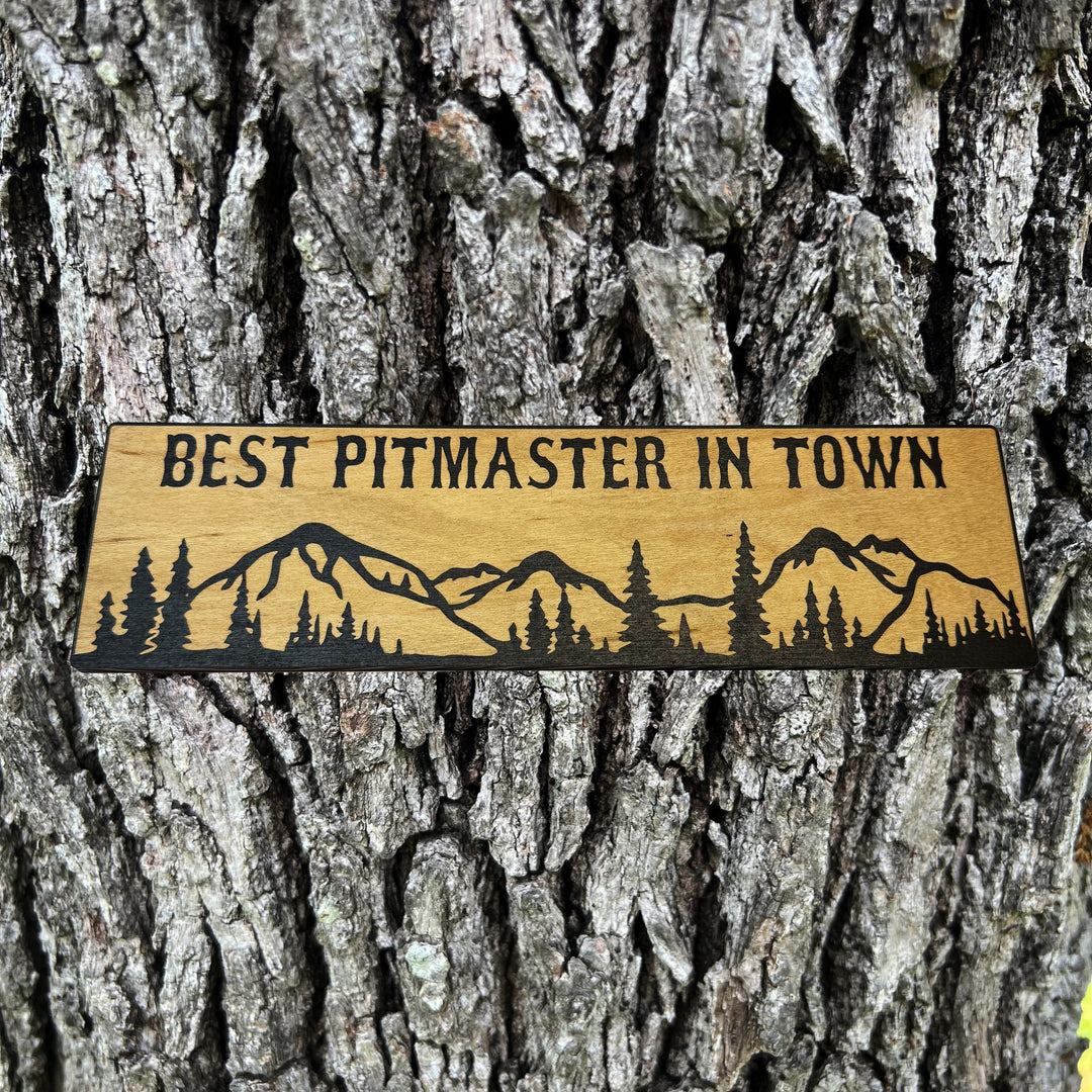 HipFlaskPlus Best Pitmaster in Town mountain scene black and natural wood sign on a tree trunk