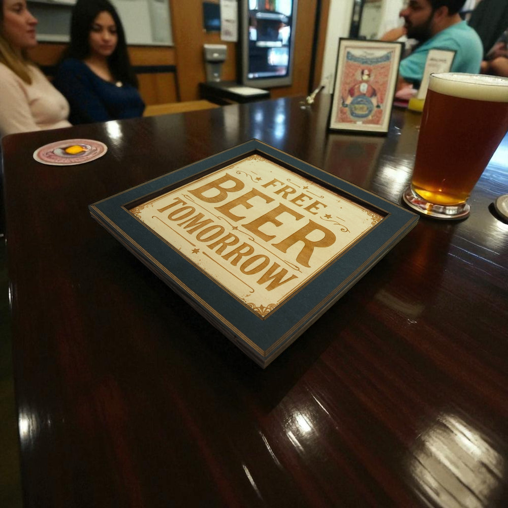 HipFlaskPlus Free Beer Tomorrow bar sign engraved wood wall art in a black frame on a bar table with a beer