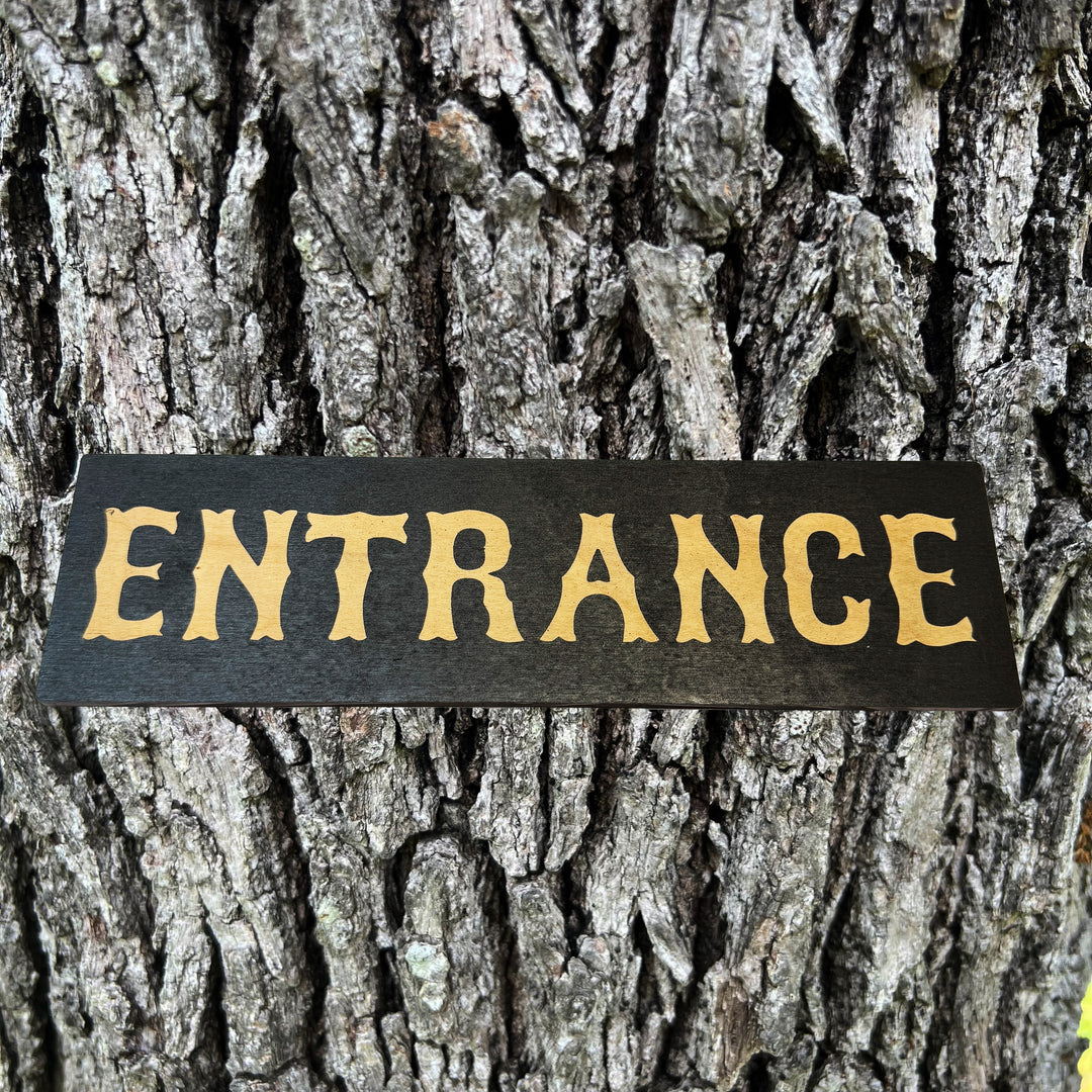 HipFlaskPlus Entrance black and natural wood sign on a tree trunk