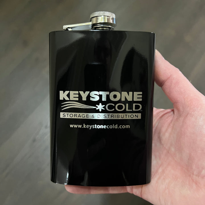 Hand holding a HipFlaskPlus black flask engraved with a custom company logo