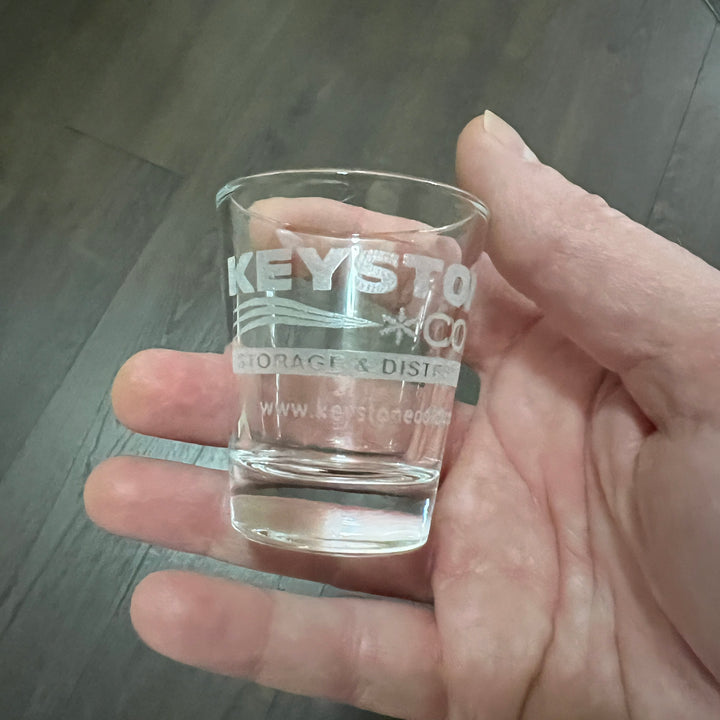 Hand holding a HipFlaskPlus shot glass engraved with a custom company logo