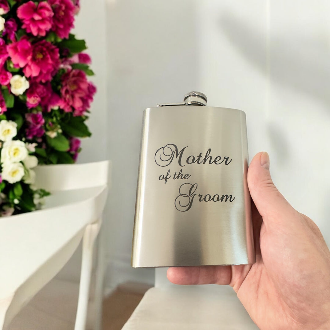 Hand holding a HipFlaskPlus 8oz stainless steel hip flask engraved with Mother of the Groom with flowers