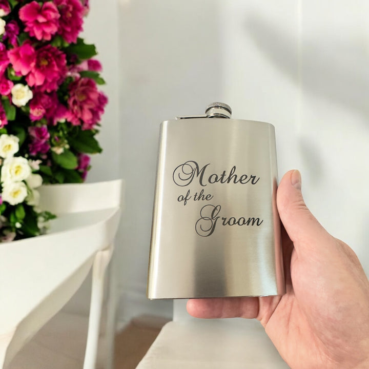 Hand holding a HipFlaskPlus 8oz stainless steel hip flask engraved with Mother of the Groom with flowers