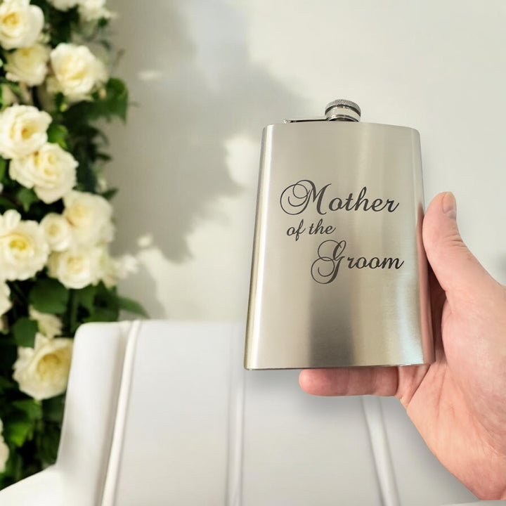 Hand holding a HipFlaskPlus 8oz stainless steel hip flask engraved with Mother of the Groom with white flowers