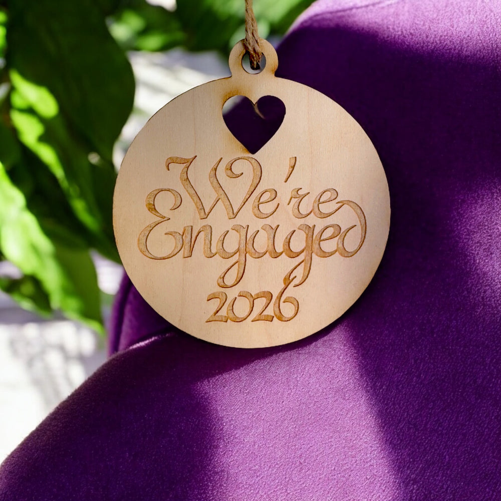HipFlaskPlus raw wood We're Engaged 2026 heart ornament on purple fabric