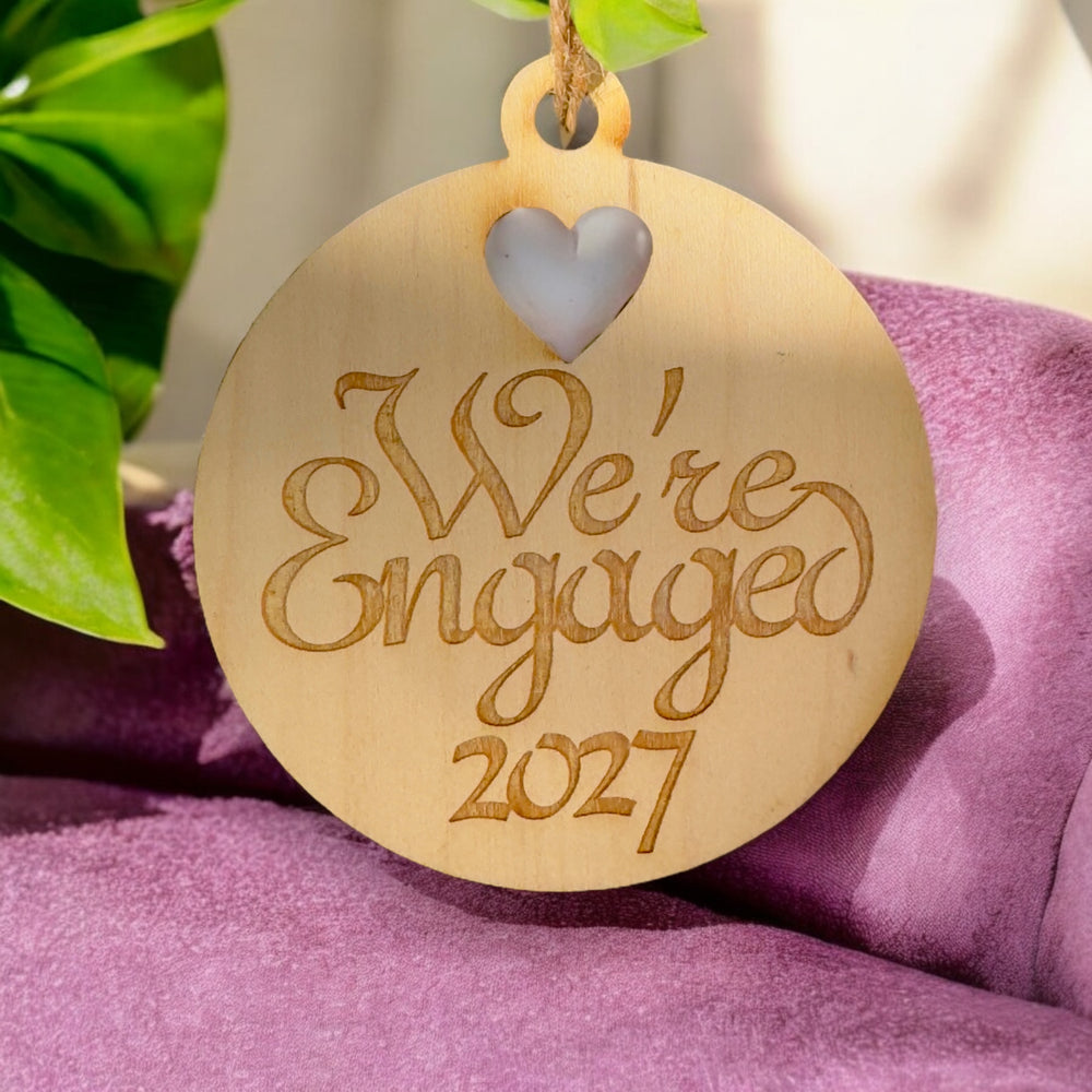HipFlaskPlus raw wood We're Engaged 2027 heart ornament on purple fabric
