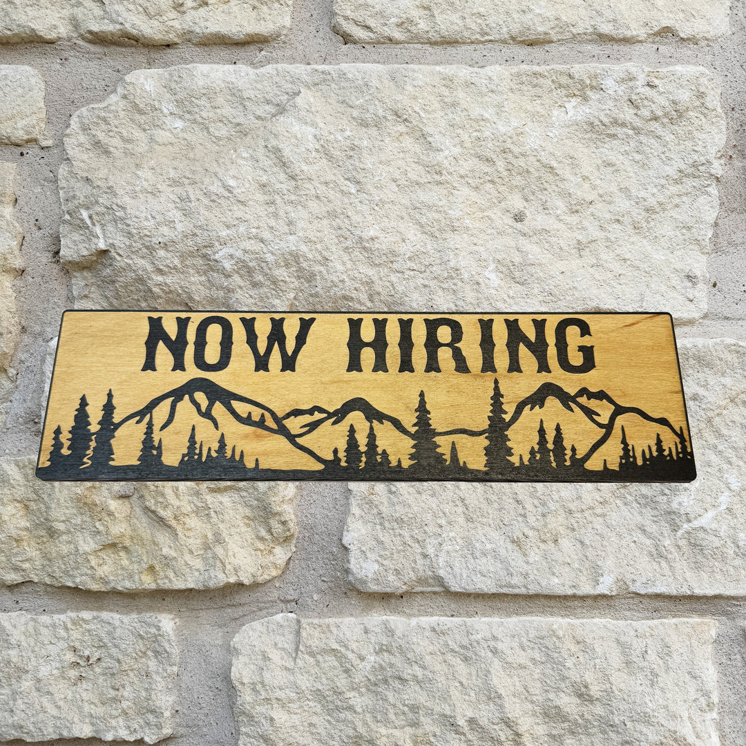 HipFlaskPlus Now Hiring mountain scene black and natural wood sign on a stone wall