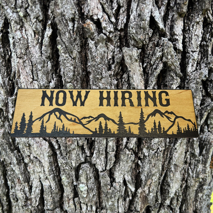 HipFlaskPlus Now Hiring mountain scene black and natural wood sign on a tree trunk
