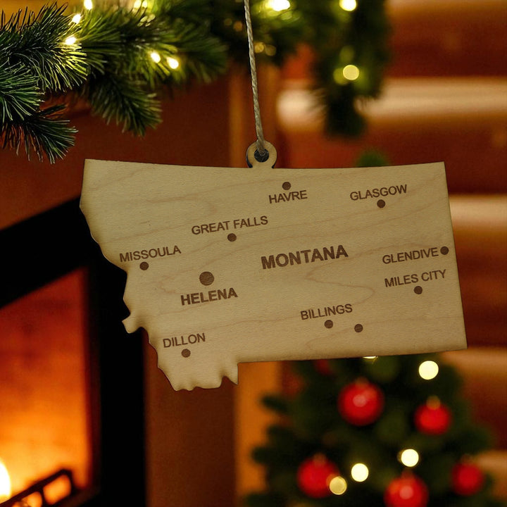 HipFlaskPlus custom Montana state ornament with cities hanging in a cozy cabin by a fireplace
