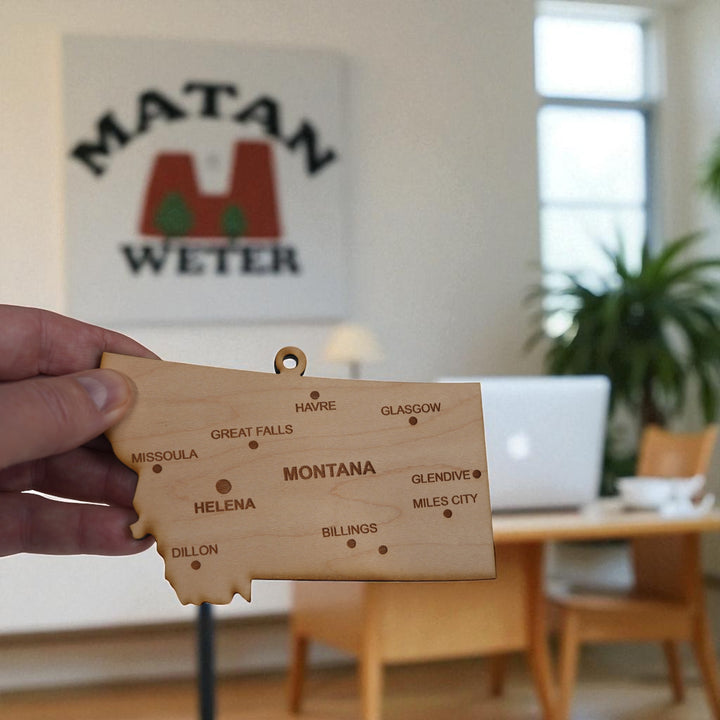 Hand holding a HipFlaskPlus custom Montana state ornament with cities in a home office