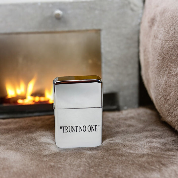 HipFlaskPlus Trust No One chrome lighter on a rug in front of a fireplace