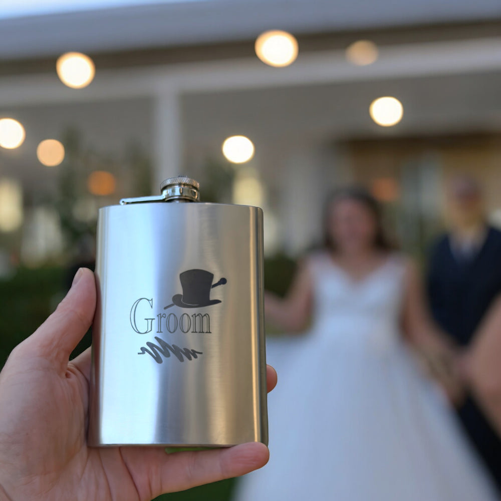 Hand holding a HipFlaskPlus 8oz stainless steel hip flask engraved with Groom top hat at a wedding