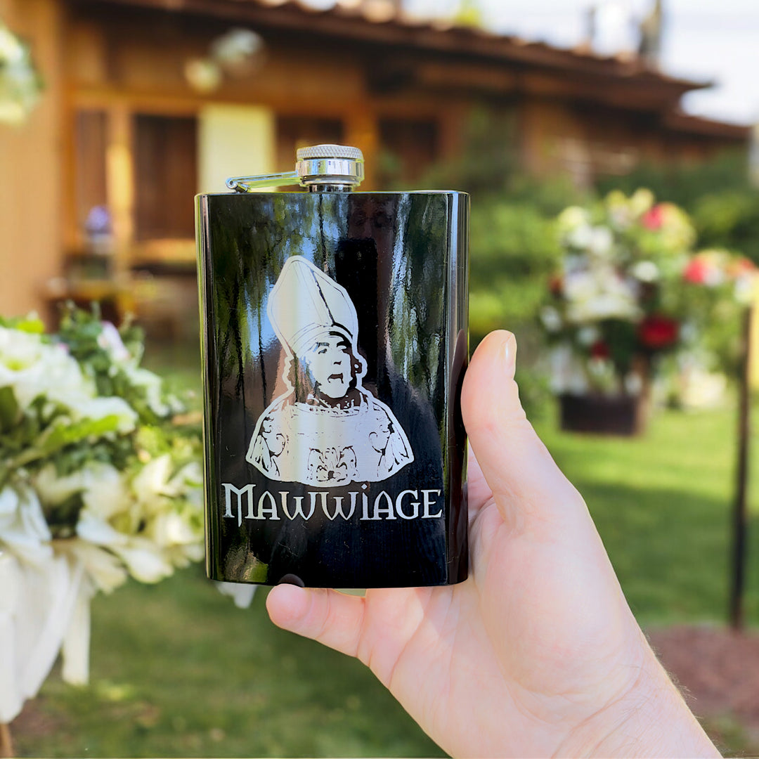 Hand holding a HipFlaskPlus 8oz black stainless steel hip flask engraved with Mawwiage bride in a garden