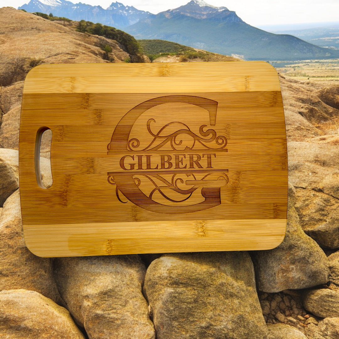 HipFlaskPlus bamboo cutting board engraved with a personalized split letter monogram and name on rocks with mountains in the background