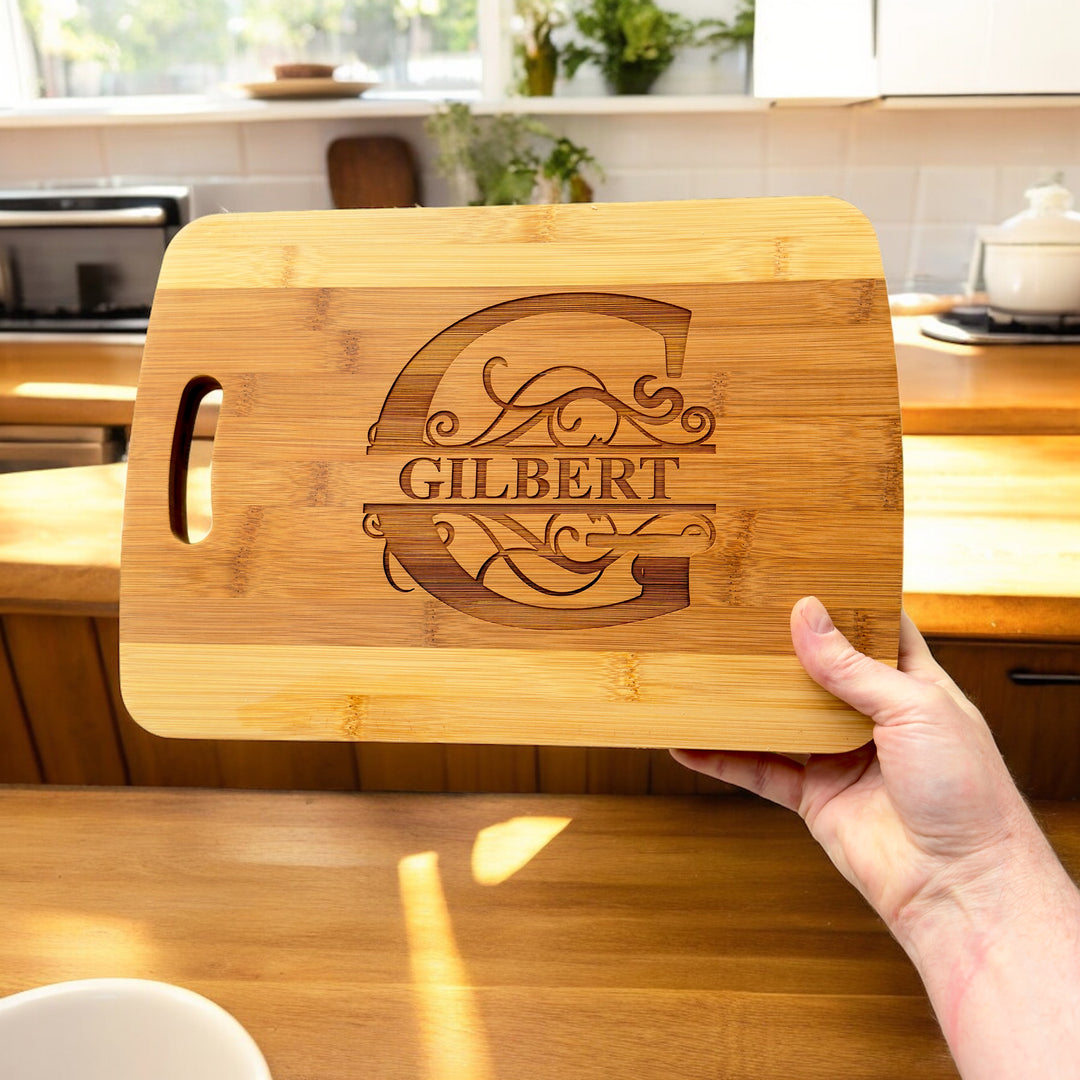 Hand holding a HipFlaskPlus bamboo cutting board engraved with a personalized split letter monogram and name in a kitchen