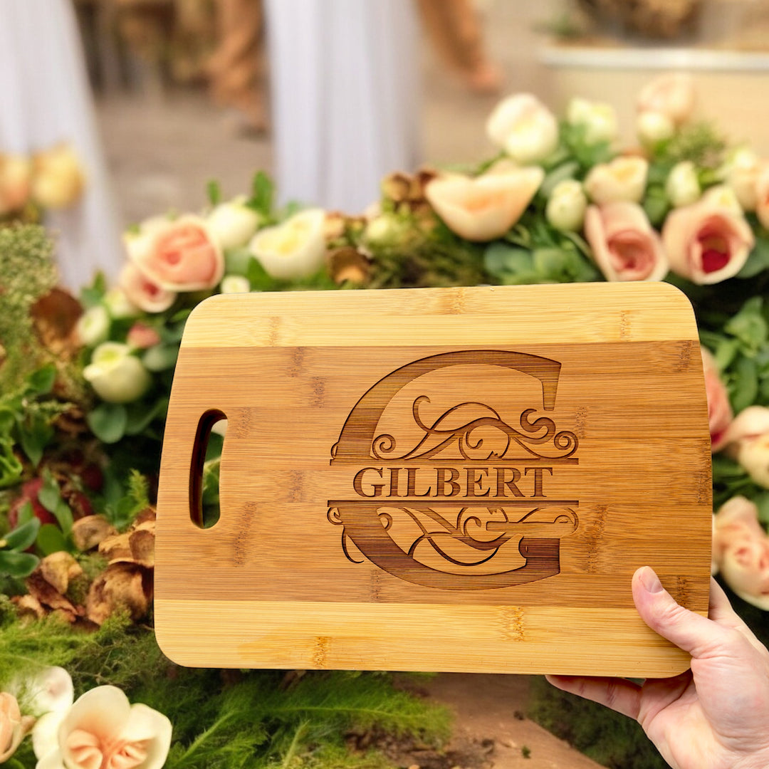 Hand holding a HipFlaskPlus bamboo cutting board engraved with a personalized split letter monogram and name above pink roses