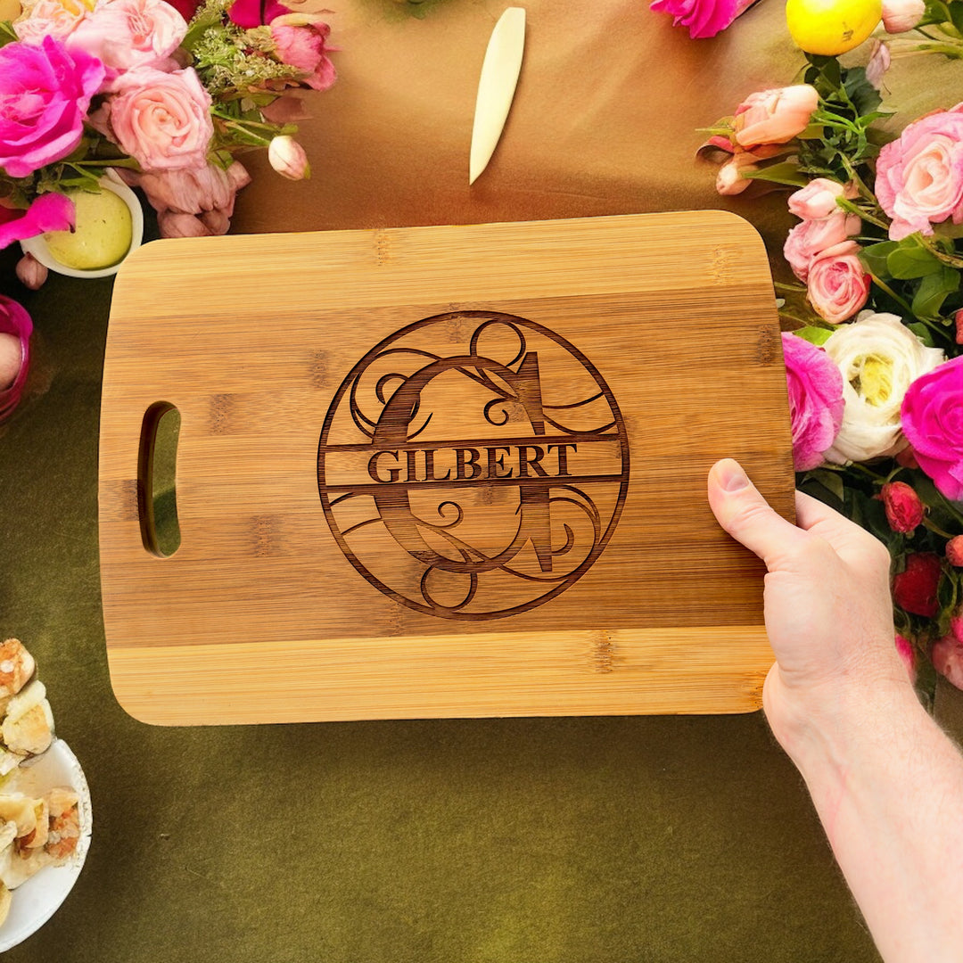 Hand holding a HipFlaskPlus bamboo cutting board engraved with a personalized split letter monogram and name above pink roses