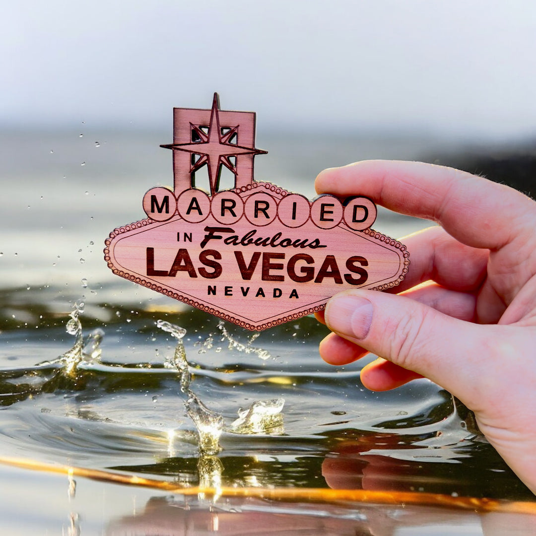 Hand holding a HipFlaskPlus cedar wood Married in Fabulous Las Vegas sign ornament over water