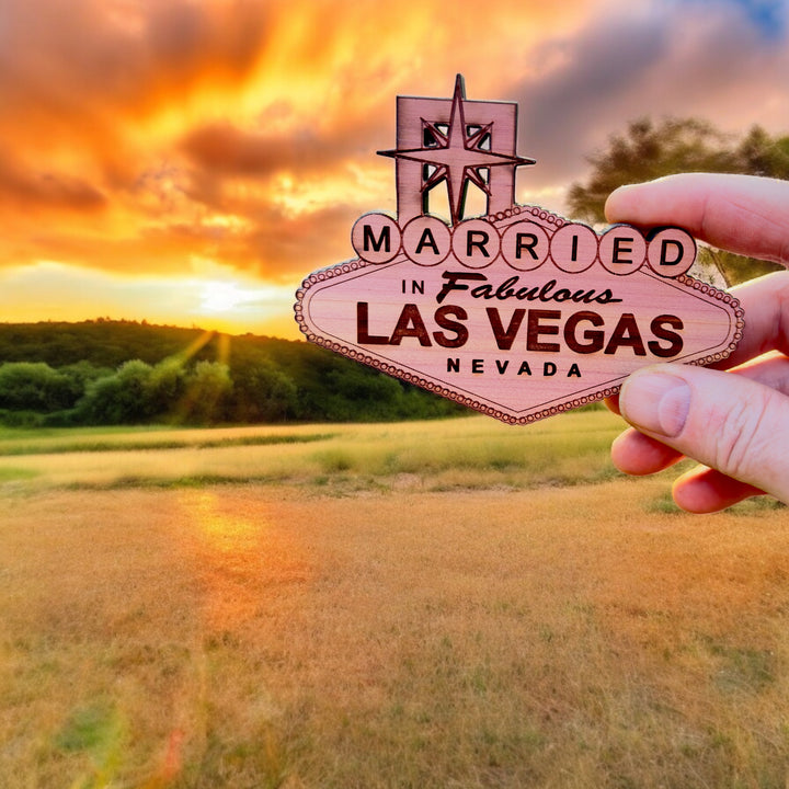Hand holding a HipFlaskPlus cedar wood Married in Fabulous Las Vegas sign ornament at sunset