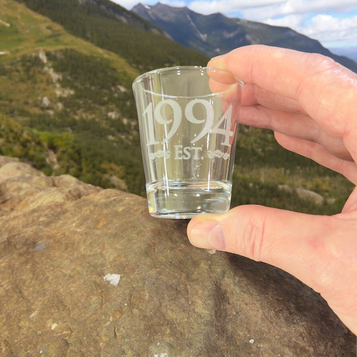 Hand holding a HipFlaskPlus Est. 1994 engraved shot glass on a mountainside