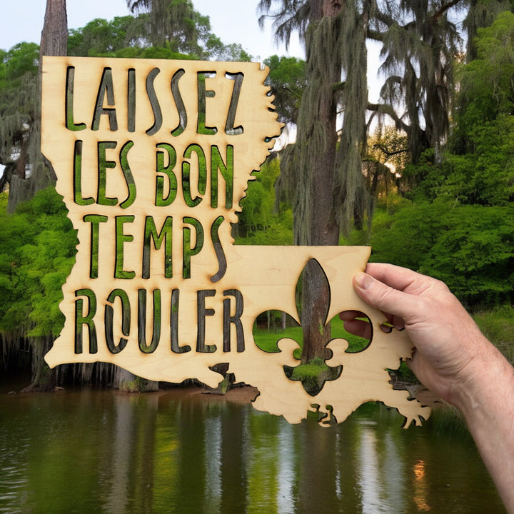 Hand holding a HipFlaskPlus Laissez les Bon Temps Rouler Louisiana maple wood cutout sign in a forest