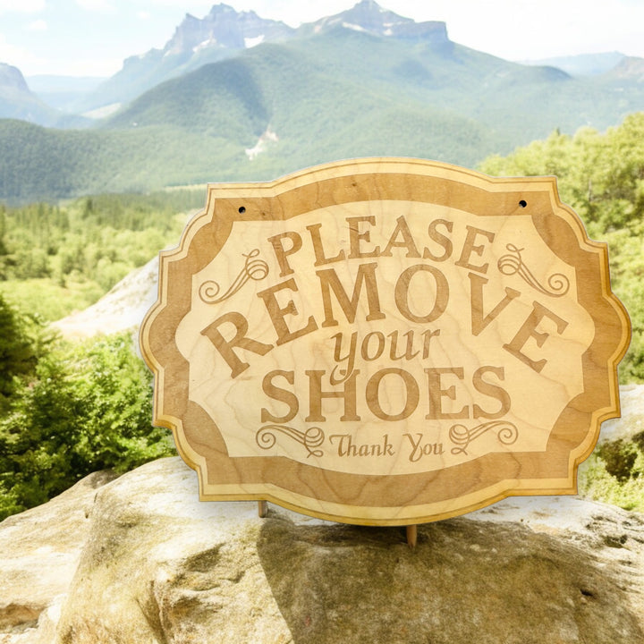 Hand holding a HipFlaskPlus Please Remove Your Shoes raw wood door sign by mountains