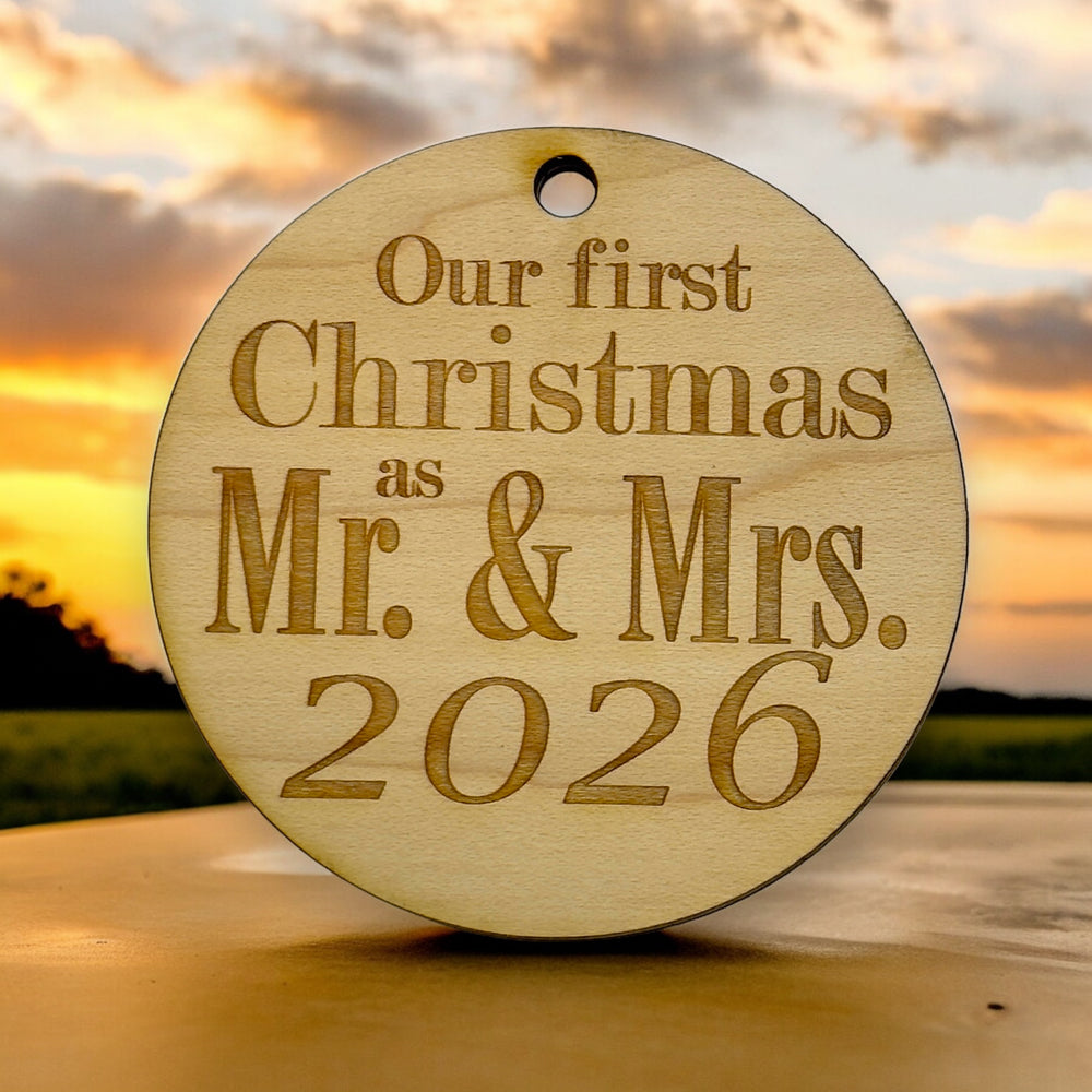 HipFlaskPlus raw wood Our First Christmas as Mr. & Mrs. 2026 ornament on a table at sunset