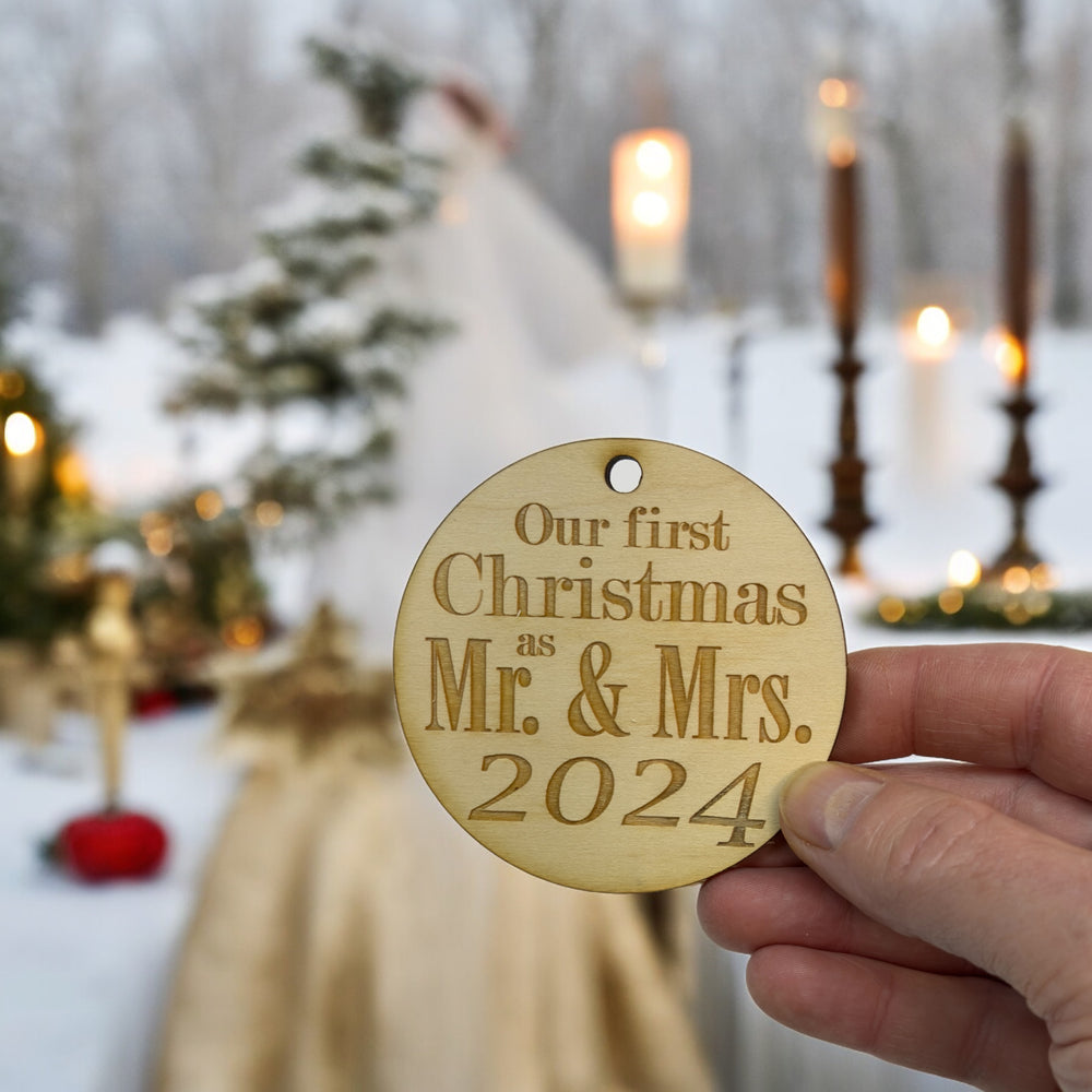 Hand holding a HipFlaskPlus raw wood Mr. & Mrs. 2024 ornament at a candlelit winter wedding