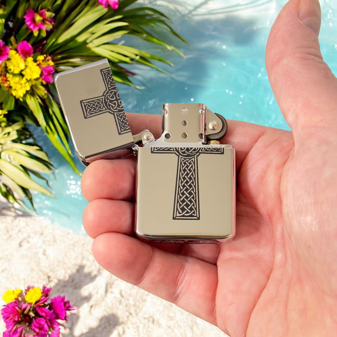 Hand holding an open HipFlaskPlus Celtic cross lighter beside a tropical pool