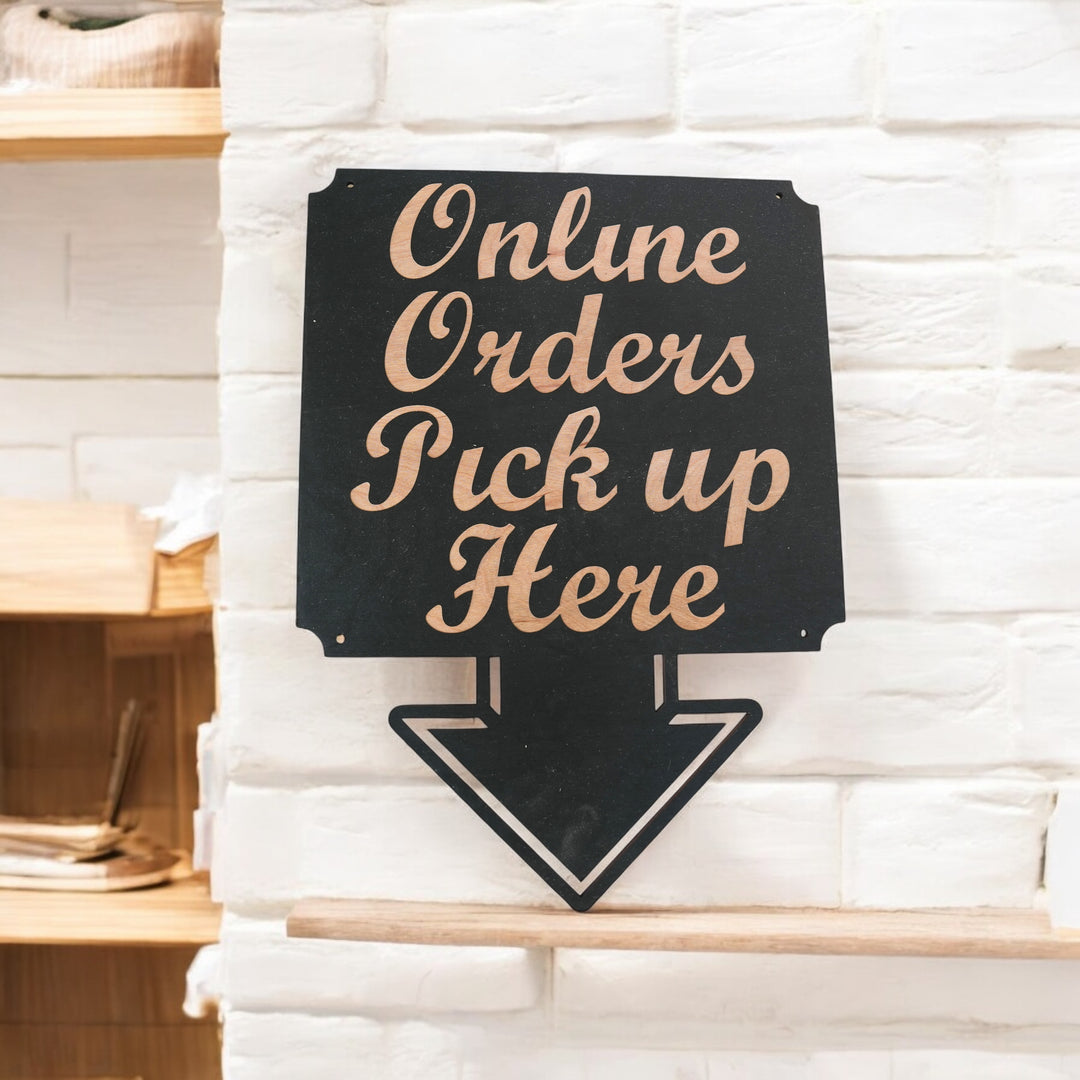 Hand holding a HipFlaskPlus Online Orders Pick Up Here black wood arrow sign by a white brick wall