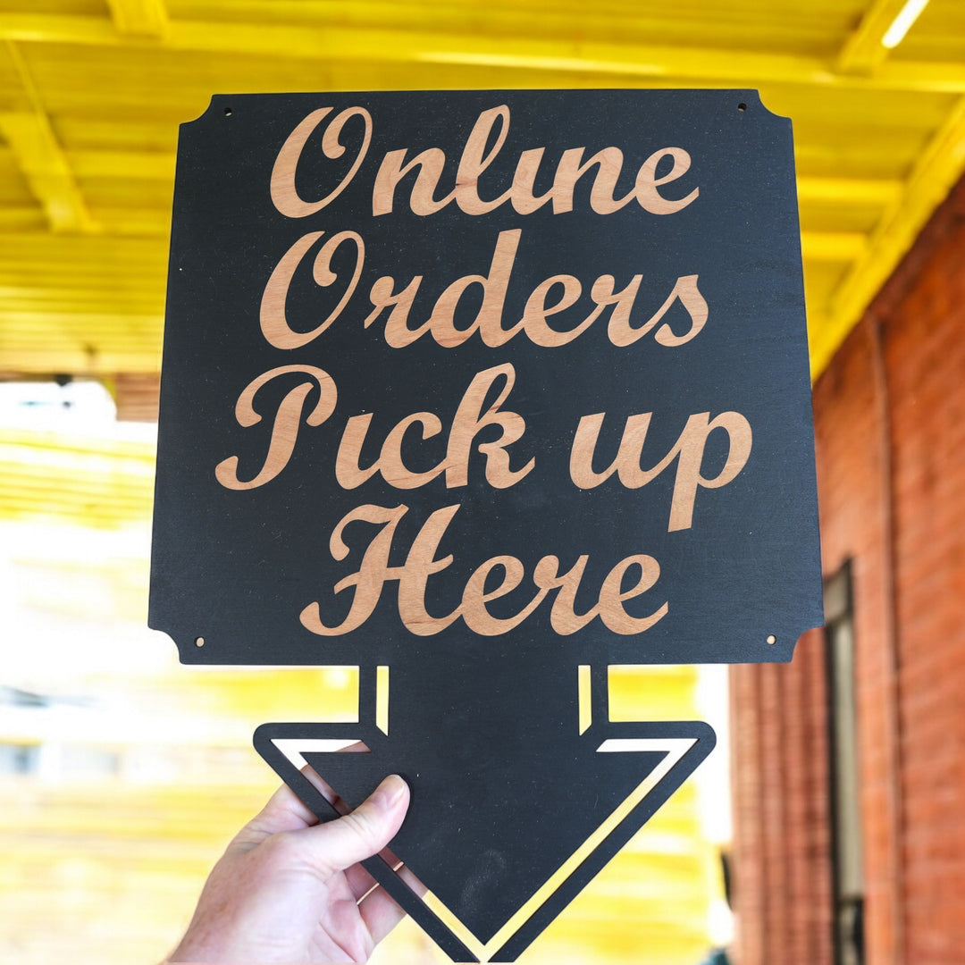 Hand holding a HipFlaskPlus Online Orders Pick Up Here black wood arrow sign by a yellow wall