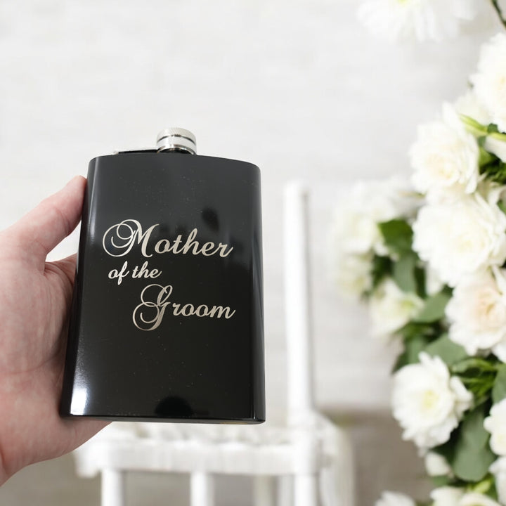 Hand holding a HipFlaskPlus 8oz black stainless steel hip flask engraved with Mother of the Groom with flowers