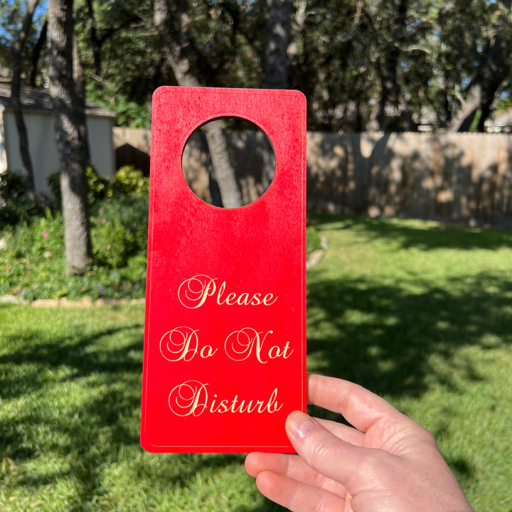 Hand holding a HipFlaskPlus red Please Do Not Disturb wood door hanger outdoors