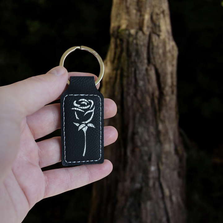 HipFlaskPlus black rectangular leatherette keychain featuring a white engraved rose design held in a hand