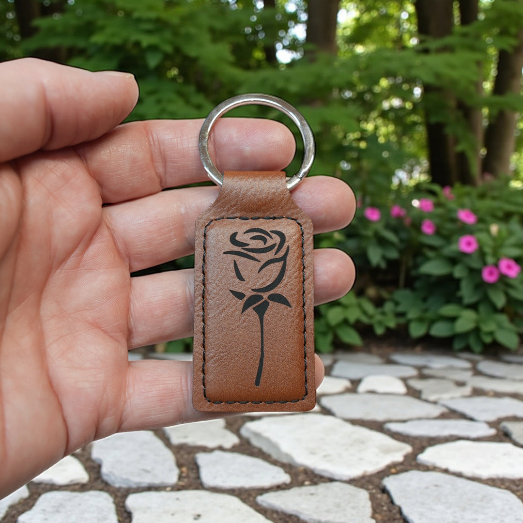 HipFlaskPlus rectangular brown leatherette keychain featuring a laser-engraved rose design held in a hand.