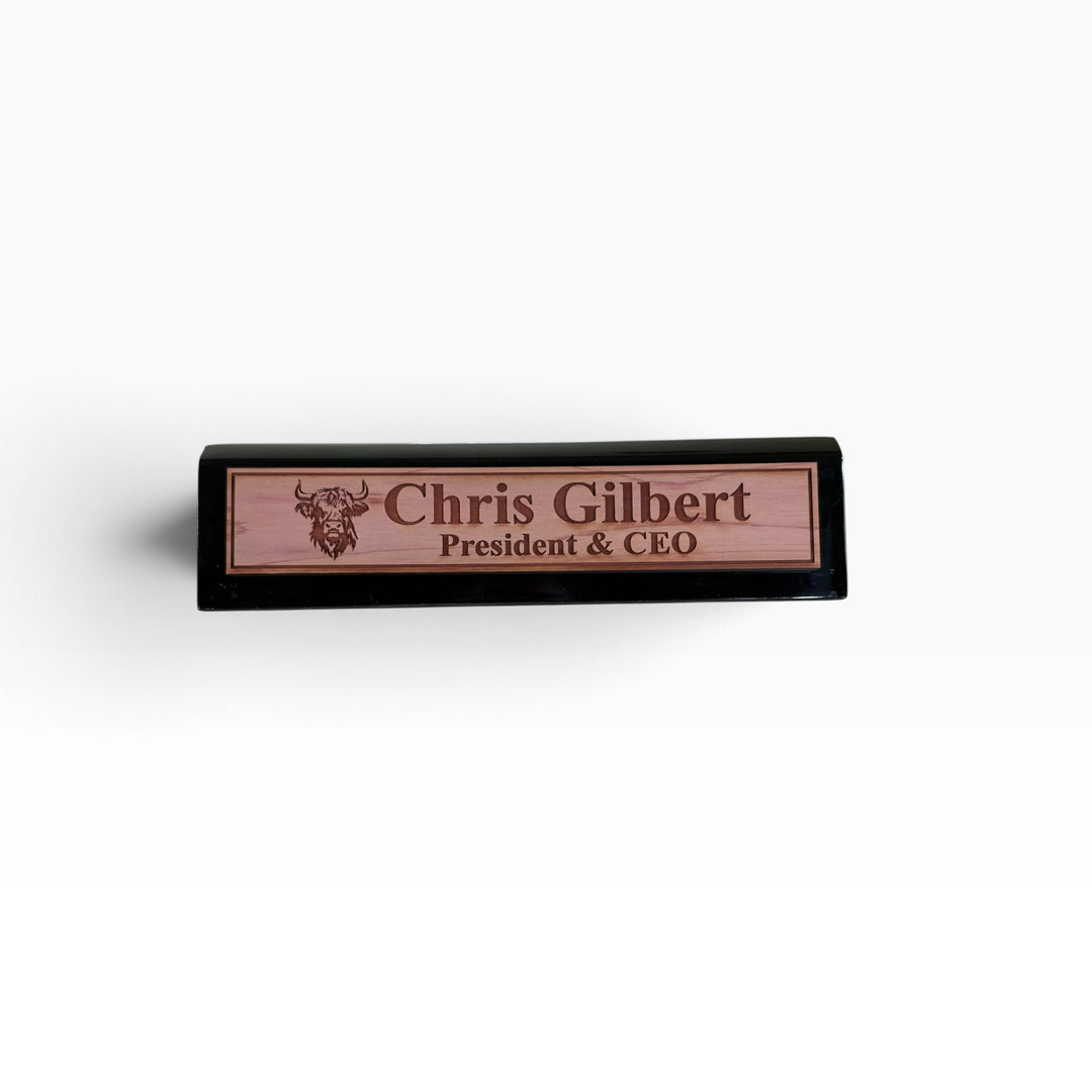 HipFlaskPlus personalized 11-inch desk wedge name plate with a Highland Cow engraving on a black piano finish base.
