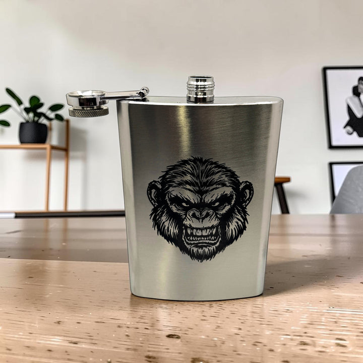 HipFlaskPlus 8oz stainless steel flask with a detailed Andy the Ape engraving and a secure hinged lid on a table.