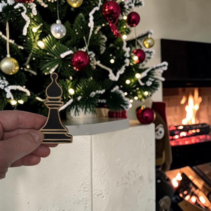 HipFlaskPlus laser-cut wooden bishop chess piece ornament held in hand in front of a decorated Christmas tree