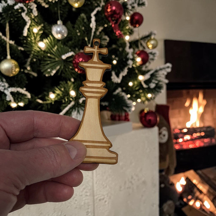 HipFlaskPlus laser-cut wooden king chess piece ornament held in hand in front of a decorated Christmas tree