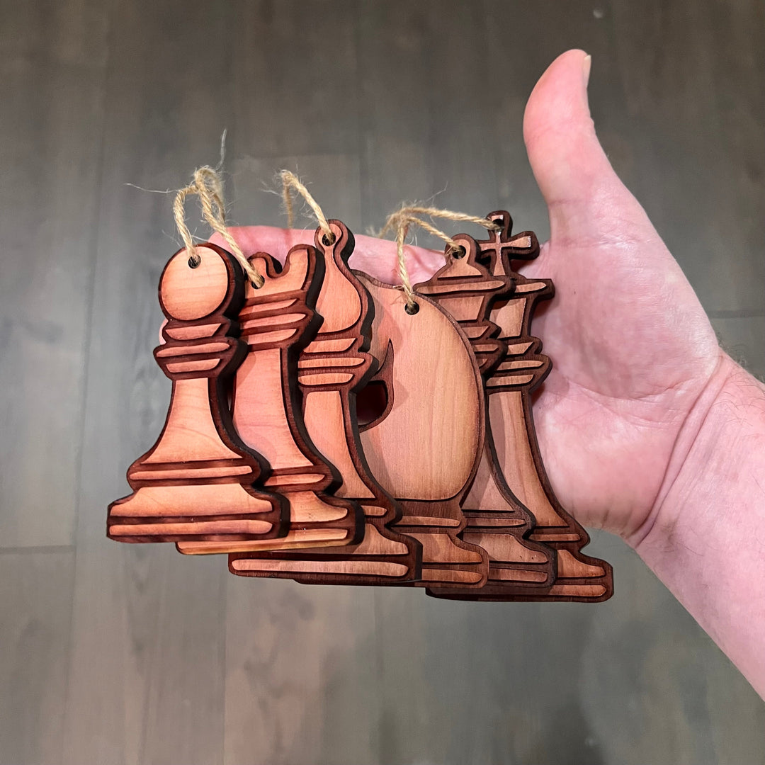 HipFlaskPlus set of 6 laser-cut wooden chess piece ornaments with rustic finish held in a hand for Christmas decor.