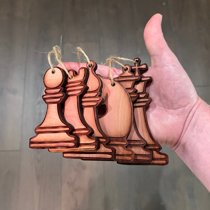 HipFlaskPlus set of 6 laser-cut wooden chess piece ornaments with rustic finish held in a hand for Christmas decor.