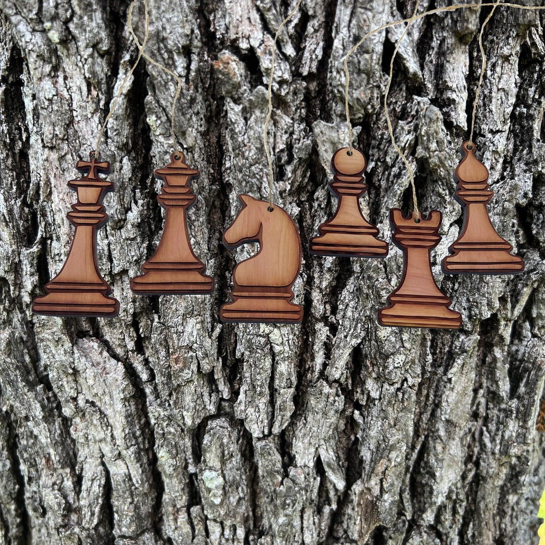 HipFlaskPlus laser engraved wooden chess piece ornaments hanging against a rustic tree bark background