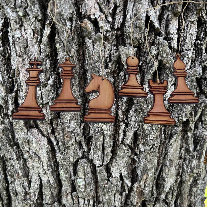 HipFlaskPlus laser engraved wooden chess piece ornaments hanging against a rustic tree bark background