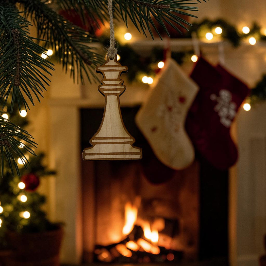 HipFlaskPlus laser-cut wooden king chess piece ornament hanging on a Christmas tree with a fireplace background