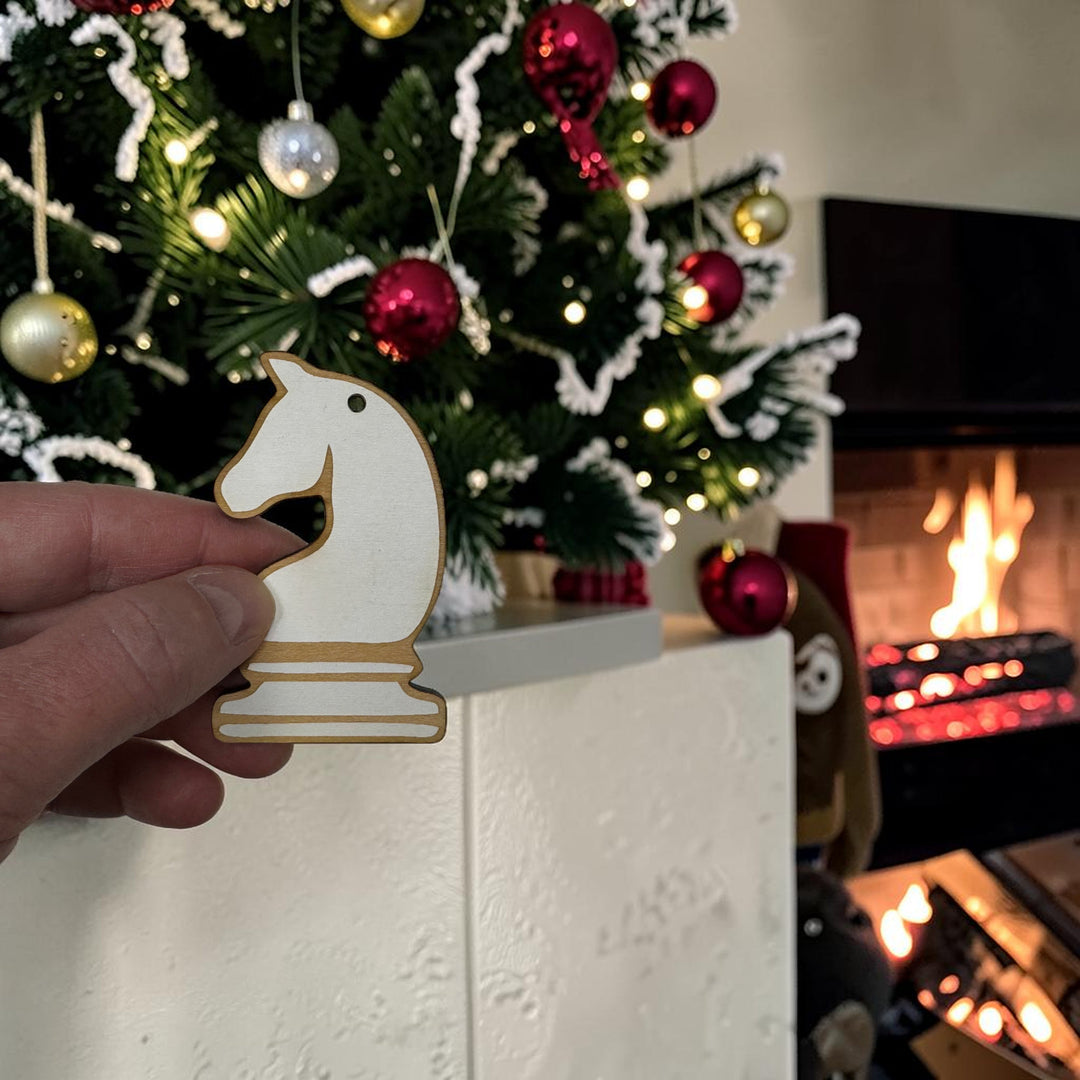 HipFlaskPlus laser-cut wooden knight chess piece ornament held in hand in front of a decorated Christmas tree