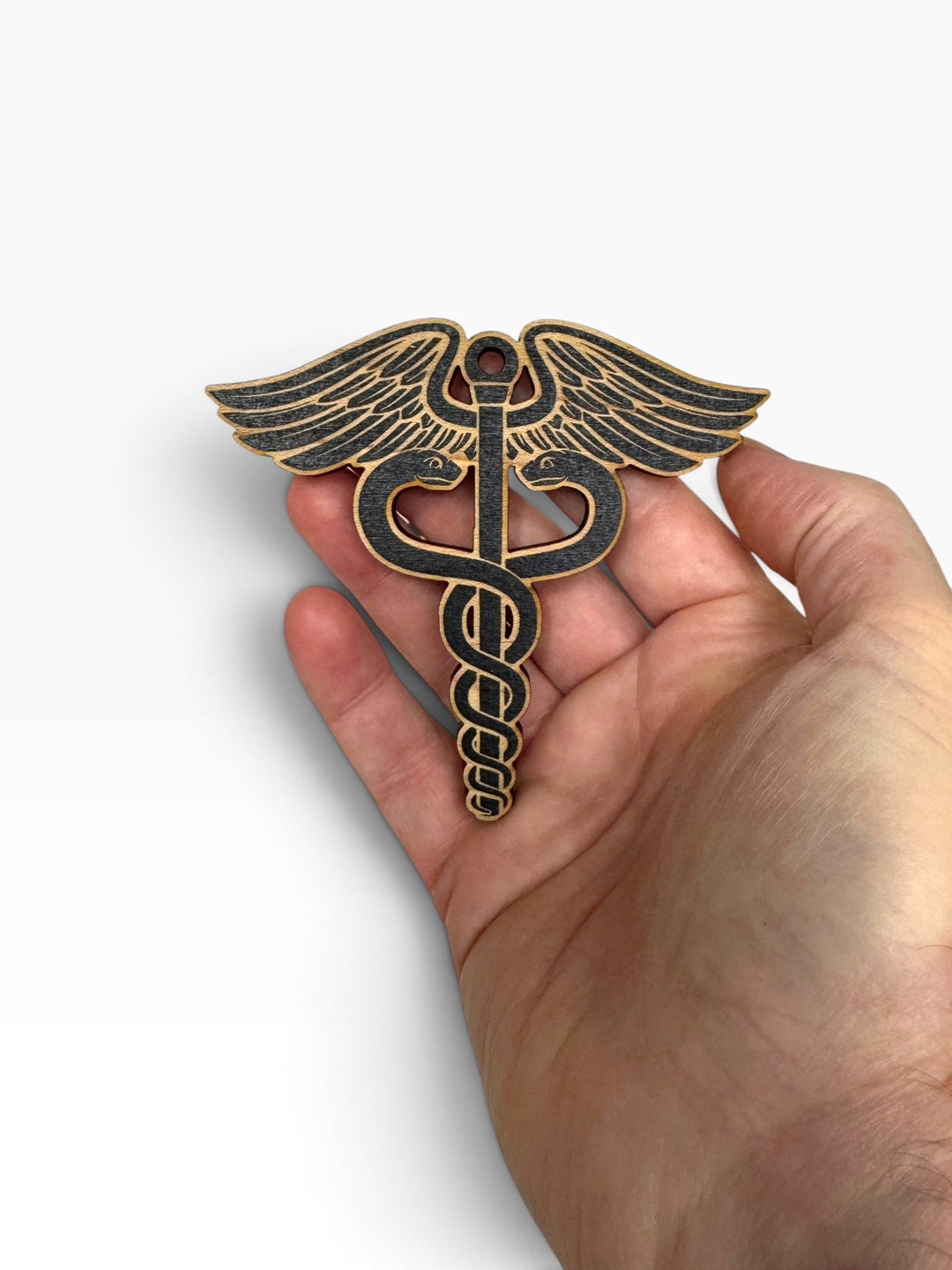 HipFlaskPlus laser-engraved wooden medical caduceus ornament held in a hand, featuring rustic wood grain details.