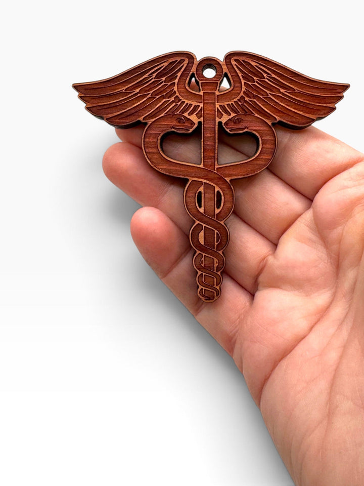HipFlaskPlus laser-engraved wooden medical caduceus ornament held in a hand, perfect for Christmas tree decoration.